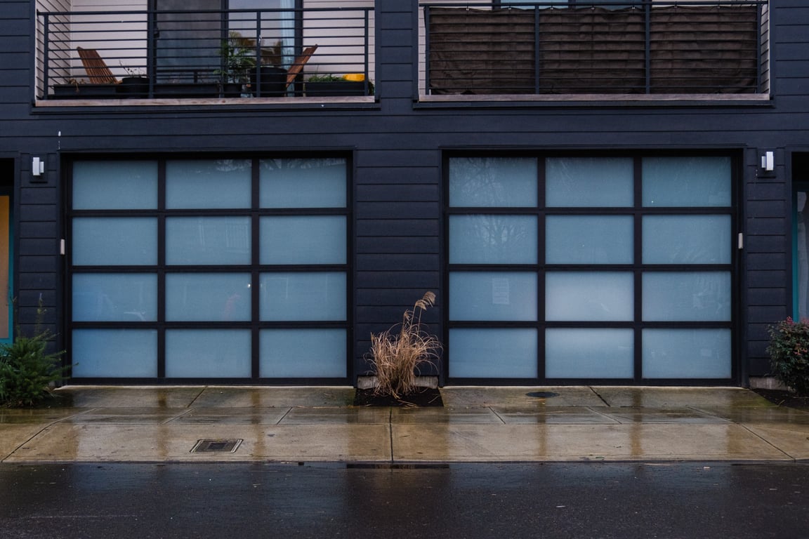 A brown plant sits in a planter in front of a blue building with tinted blue glass garage doors. It&rsquo;s wet.